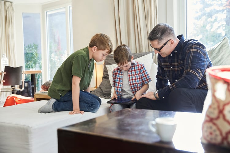 Due ragazzini con il padre sul divano, guardano qualcosa su un tablet.