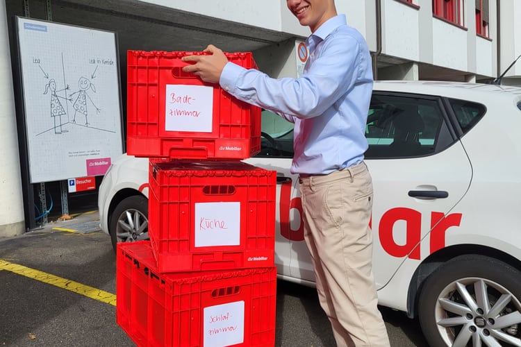 Ein junger Mann stapelt Umzugskisten der Mobiliar.