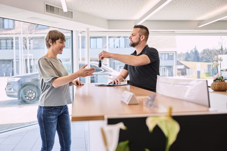 Image symbolisant la location de voiture: une femme est debout à un guichet et tend la main pour prendre une clé de voiture.