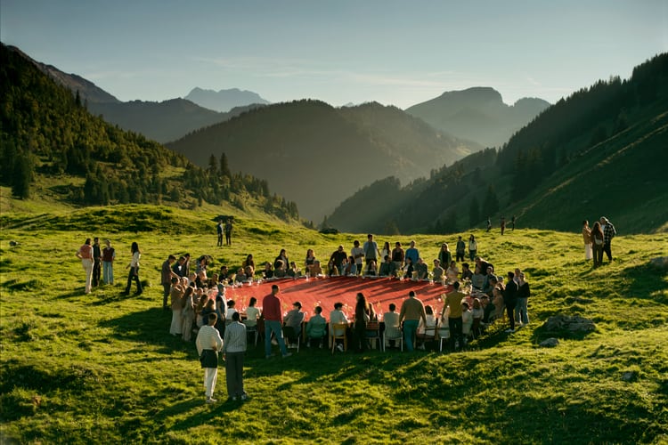 Eine Gruppe von Leuten sitzen an einem grossen roten runden Tisch auf einer grünen Wiese