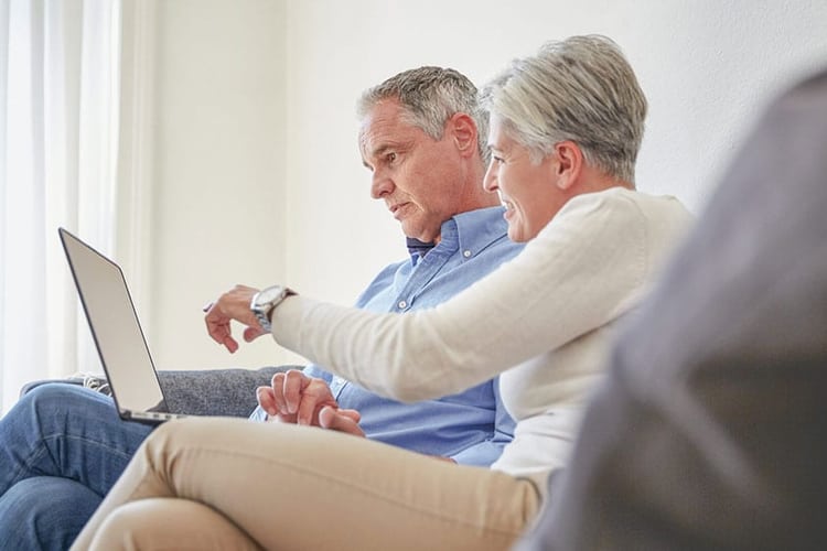 Ein älteres Paar auf dem Sofa, in einen Laptop schauend