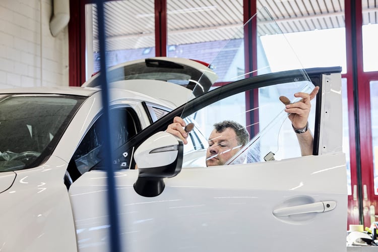 Ein Mann installiert eine Autoscheibe in einem weissen Fahrzeug. Symbolbild für mangehlafte Autoreparatur. 