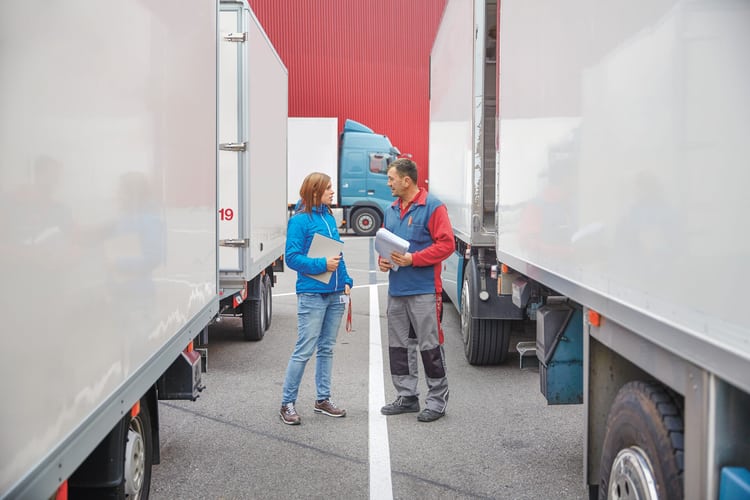 Ein Mann und eine Frau stehen zwischen zwei Lastwagen und besprechen etwas. 