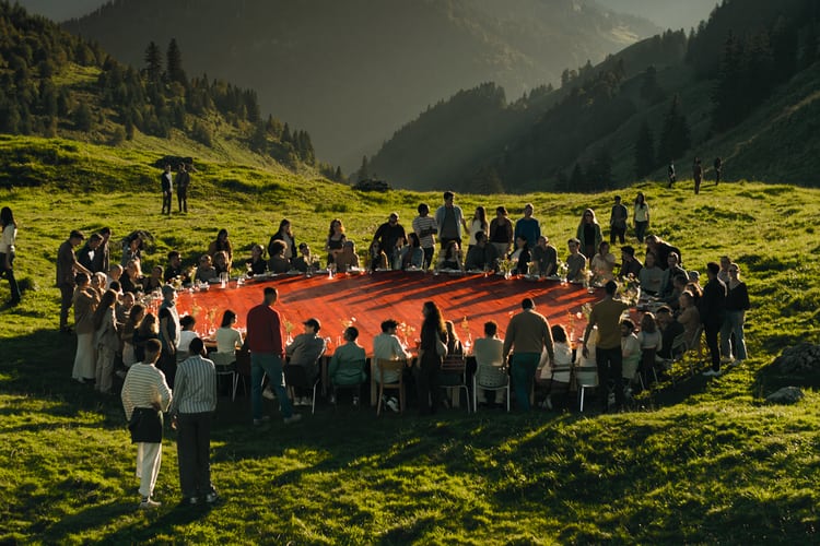 Une grande table rouge dans la nature autour de laquelle de nombreuses personnes sont assis.