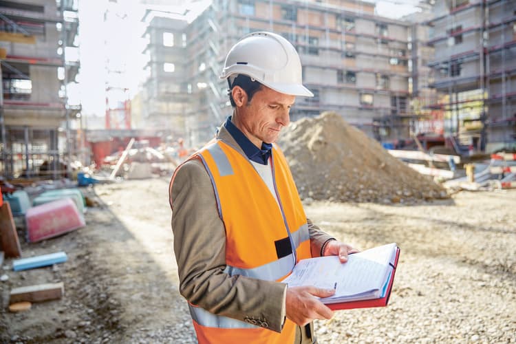 Un uomo col casco in cantiere tiene una check list in mano. 