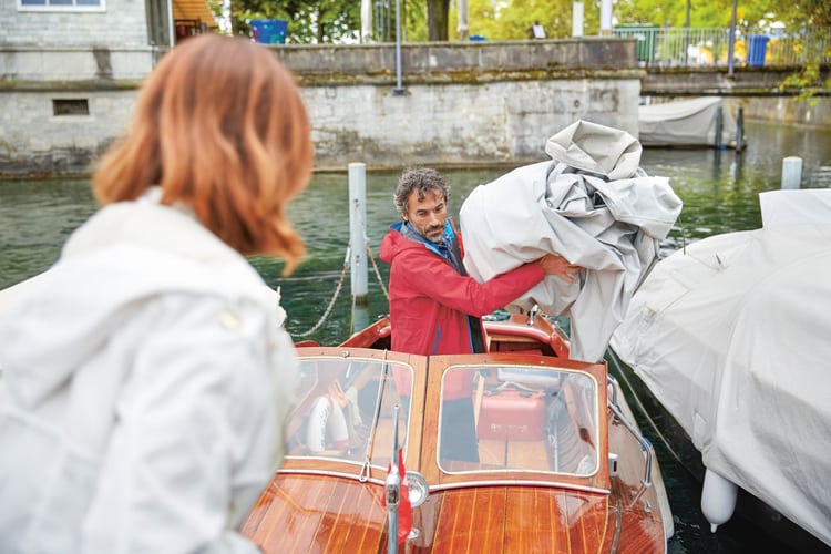 Vu du quai, un homme ôte la bâche de son bateau à moteur. Au premier plan se tient une femme qui s’apprête à l’aider. 