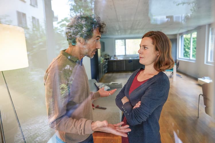 Un uomo e una donna sono in piedi in un appartamento e discutono animatamente: l’uomo gesticola, mentre la donna ascolta a braccia conserte. Un’immagine simbolica della tematica del divorzio e della separazione.