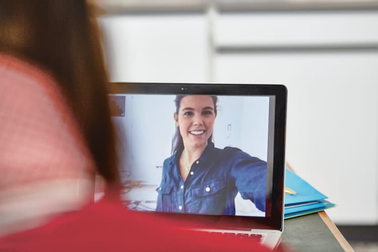 Une femme souriante apparaît sur l'écran d'un ordinateur portable. Image symbolique du love scamming.