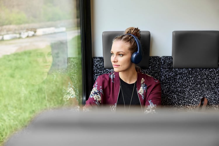 C’è una donna seduta sul treno con le cuffie.