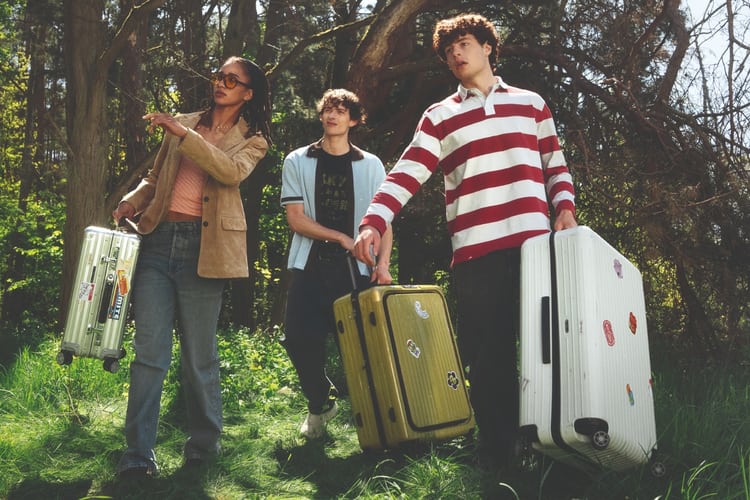 Trois jeunes adultes se promènent dans la nature avec leurs valises et une femme montre le lointain.