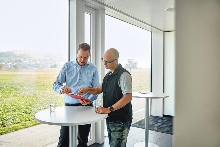 Deux hommes discutent autour d’une petite table haute.