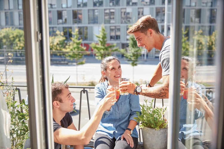 Drei junge Personen stossen mit Getränken auf einem Balkon an. Symbolbild für Solidarmiete.