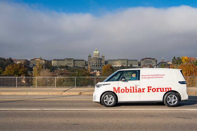 Une camionnette blanche portant l’inscription Mobiliar Forum traverse le Monbijoubrücke. À l’arrière-plan, on aperçoit le Palais fédéral.