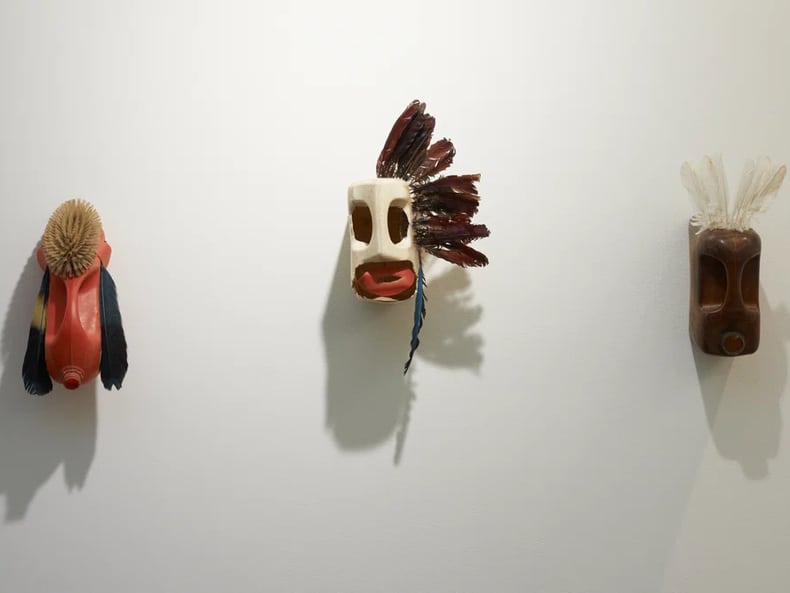 tre maschere sui volti alla parete nella mostra Arte e sostenibilità presso la Mobiliare