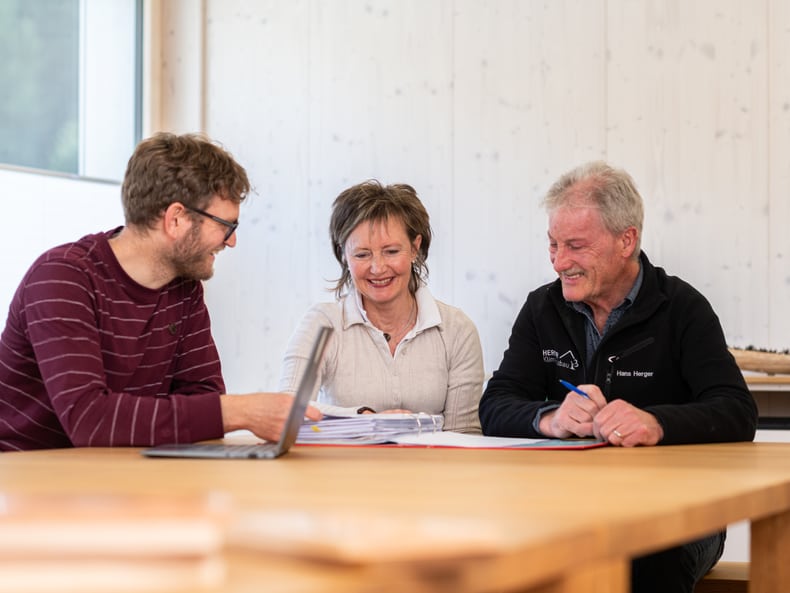 Un conseiller en assurances de la Mobilière mène un entretien de conseil avec deux clients. Toutes les personnes discutent autour d’une table en bois. 