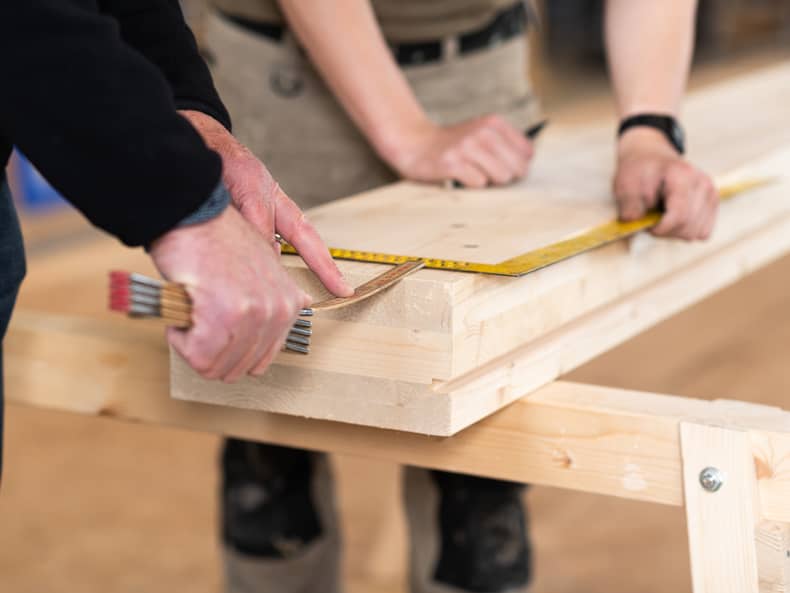 Deux personnes prennent les dimensions d’une poutre en bois. 