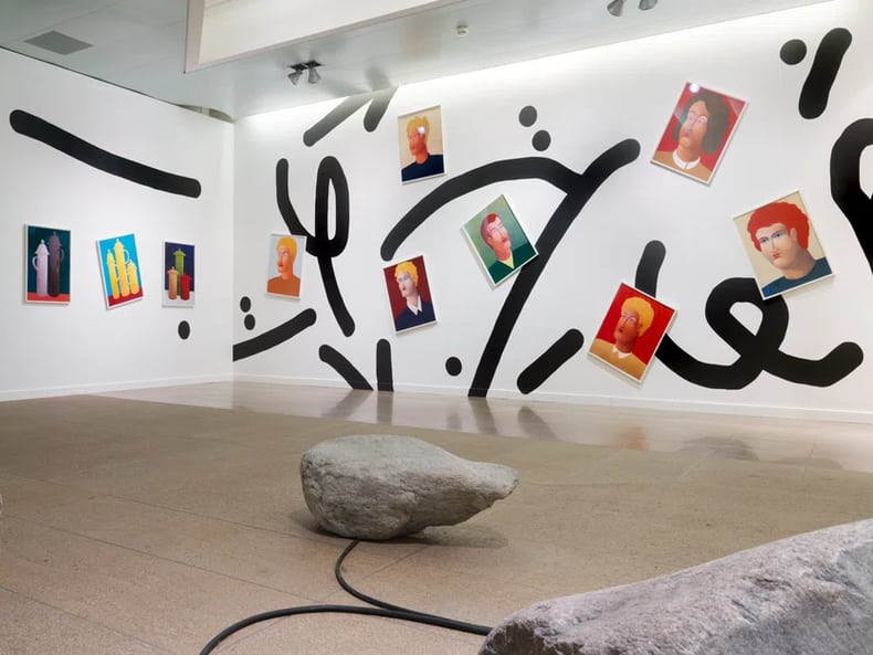 Wand mit schwarzen Formen und Bildern von Köpfen in der Kunstausstellung der Mobiliar