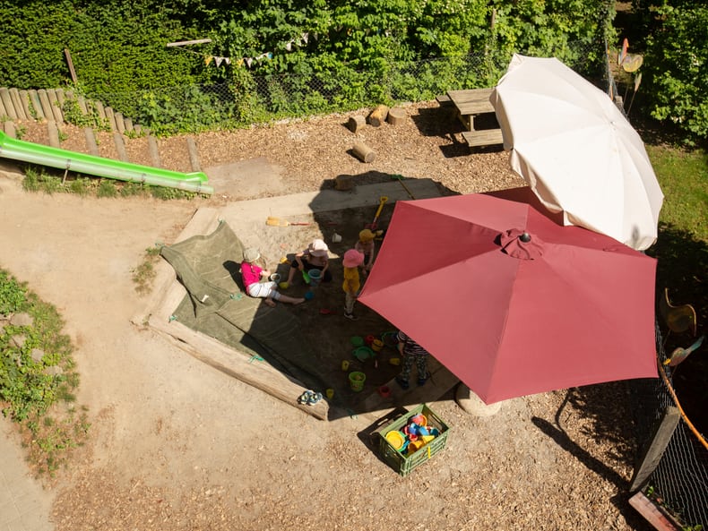 Spielende Kinder im Sandkasten werden geschützt von Sonnenschirme