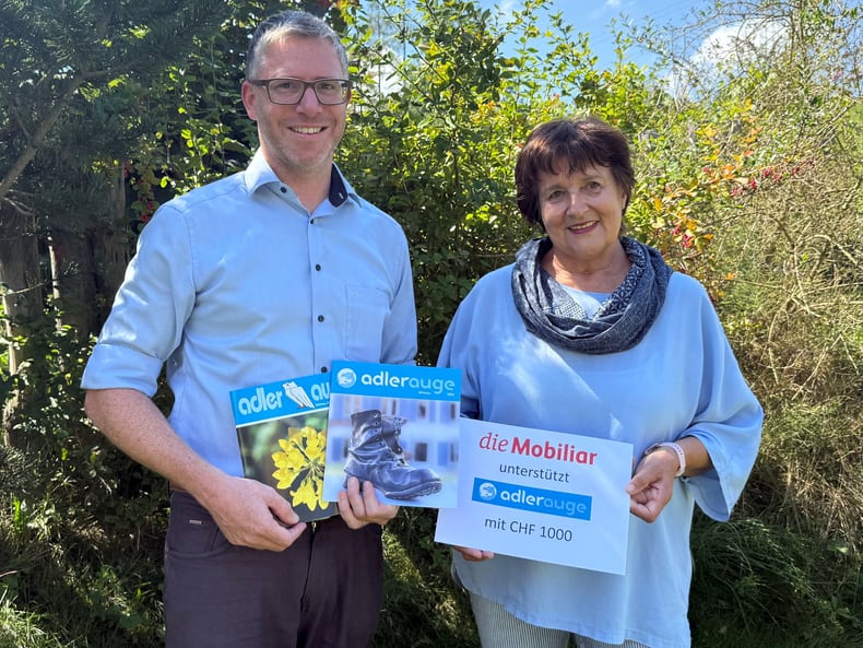 2 Personen halten einen Mobiliar-Check und 2 Adlerauge Magazine.