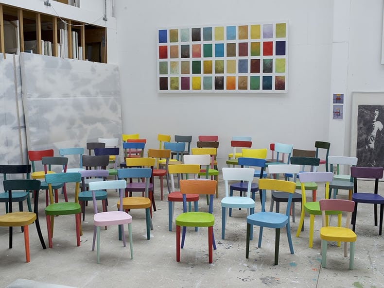 sedie colorate davanti a una parete con campi colorati nella mostra Arte e sostenibilità presso la Mobiliare 