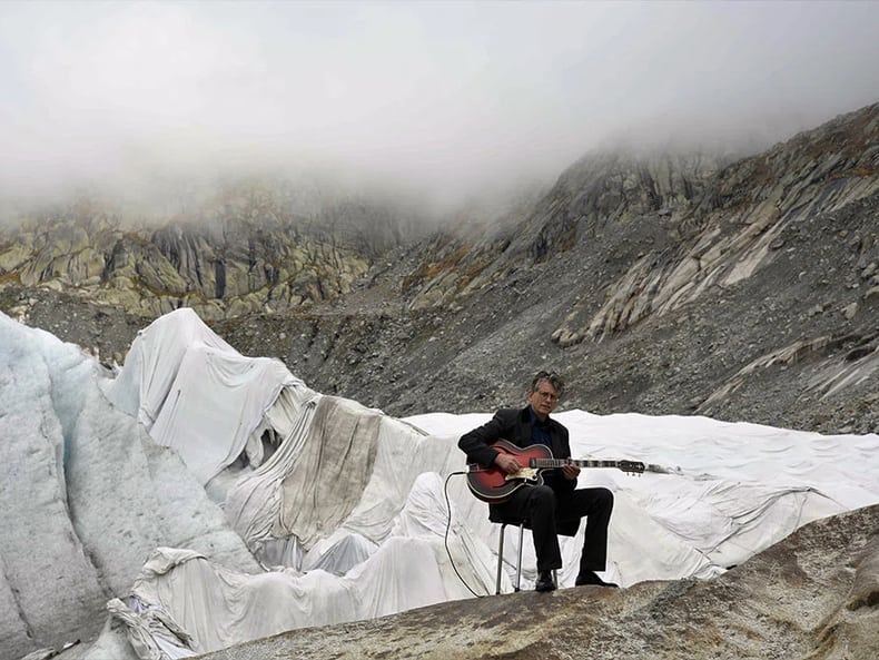 Mann vor Gletscher spielt Gitarre in der Ausstellung Kunst und Nachhaltigkeit in der Mobiliar 