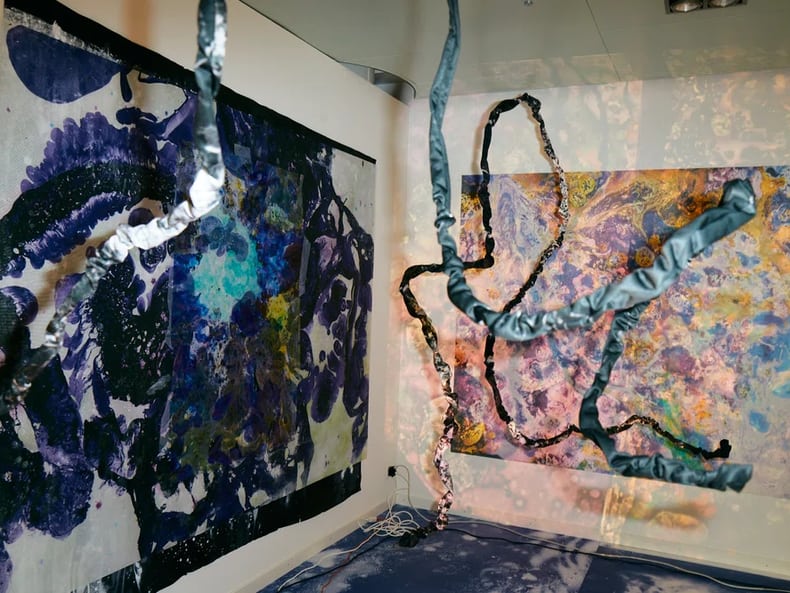 Dipinti colorati preceduti da due forme, nella mostra Arte e sostenibilità presso la Mobiliare 