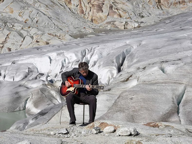 Mann auf Gletscher spielt Gitarre in der Ausstellung Kunst und Nachhaltigkeit in der Mobiliar 