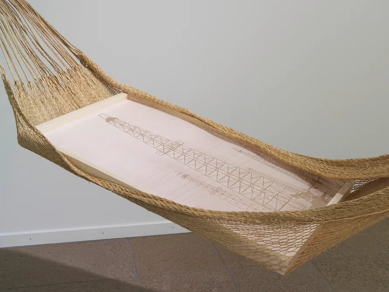 Foto di un palo elettrico in un’amaca in tessuto marrone nella mostra Arte e sostenibilità della Mobiliare 