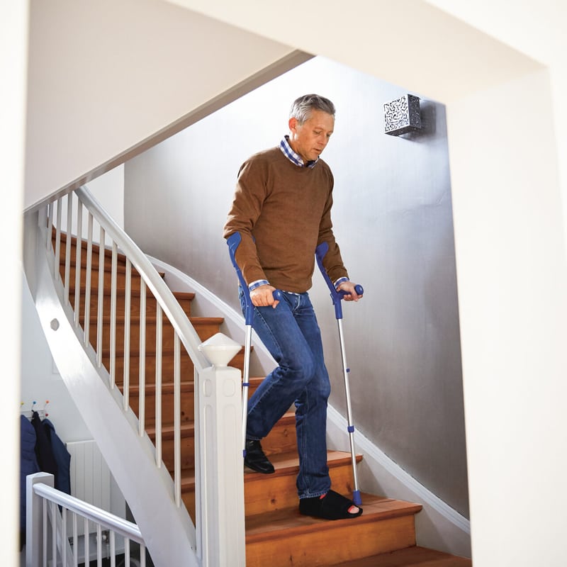 Un homme d’âge moyen descend les escaliers d’un appartement à l’aide de béquilles.