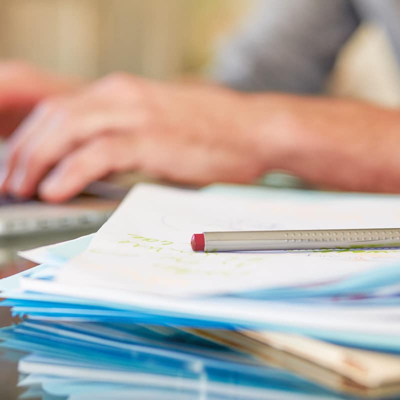 Un homme à l’ordinateur à côté d’une pile de papier.