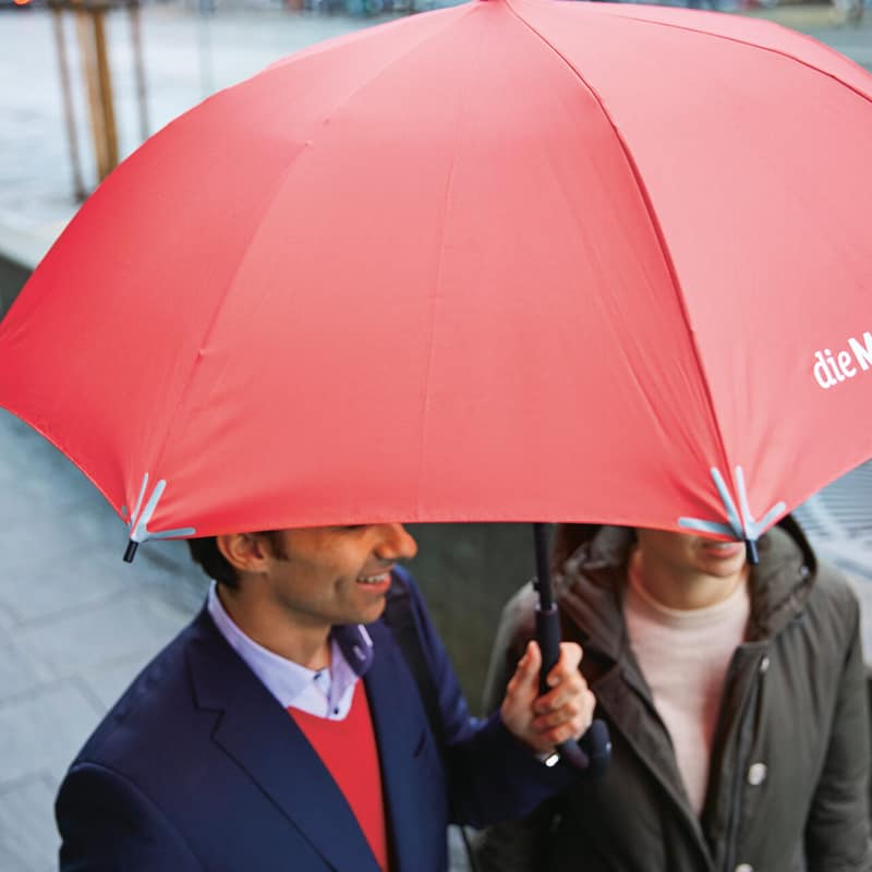 Zwei Personen gehen mit einem Mobiliar Regenschirm durch den Regen
