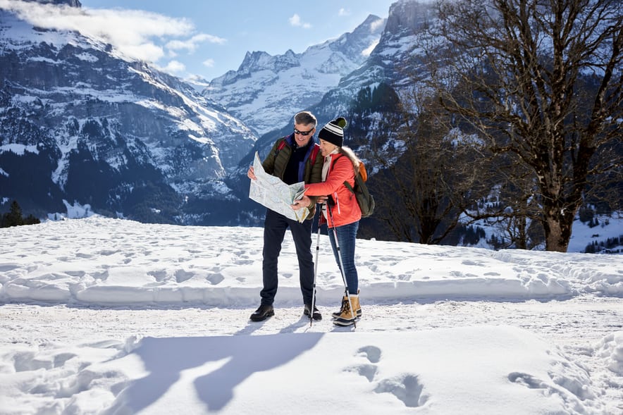 Un couple marche dans la neige et s’oriente sur une carte