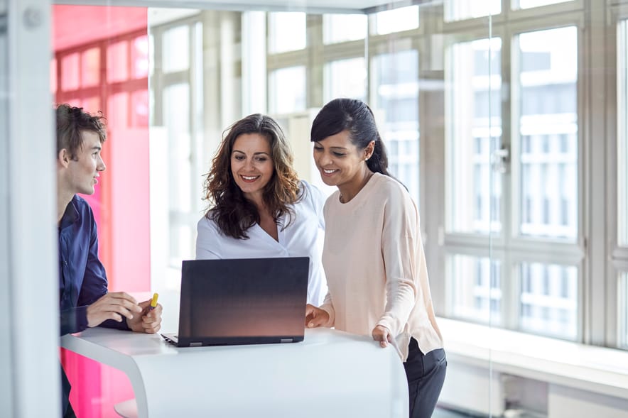 zwei Frauen und ein Mann schauen sich etwas auf einem Notebook an