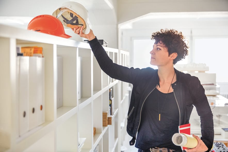 Un architetto prende da un guardaroba un casco bianco per metterlo.