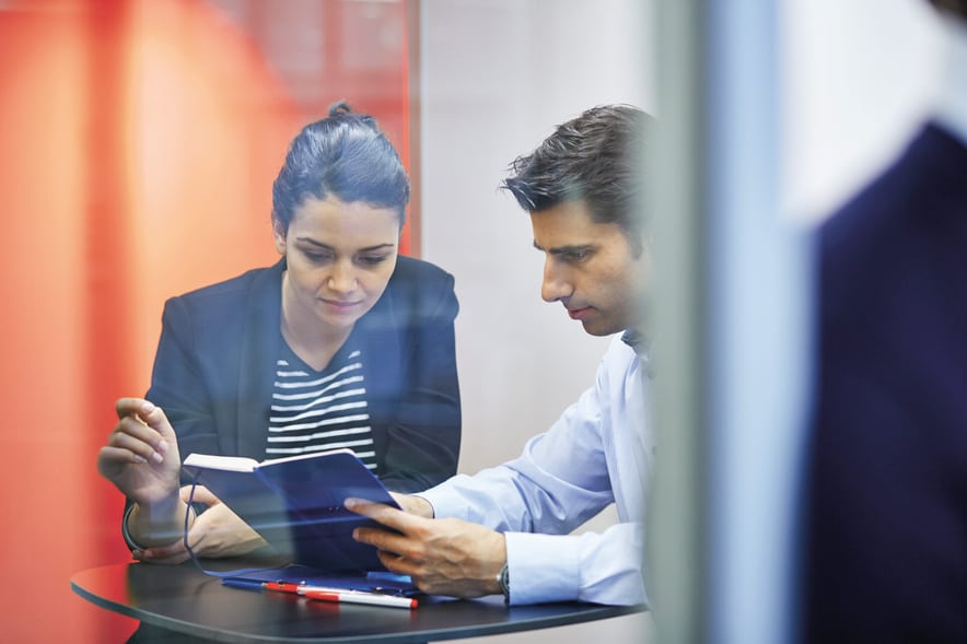 Una donna e un uomo discutono il contenuto di un taccuino che tengono davanti a sé.