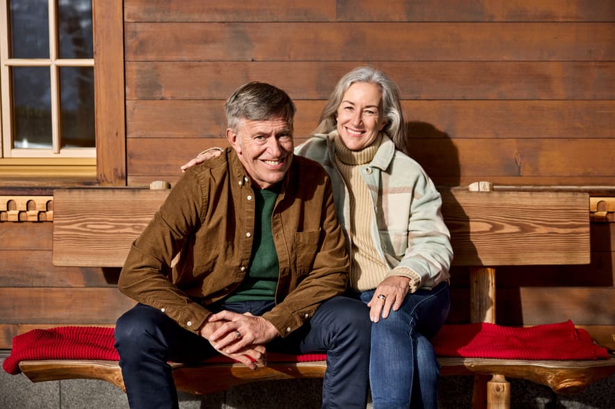 Älteres Paar sitzt draussen auf Bank vor Holzwand