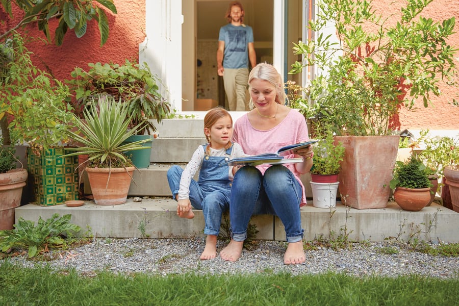 Madre e figlia sono sedute sulle scale che portano in giardino e guardano un libro.