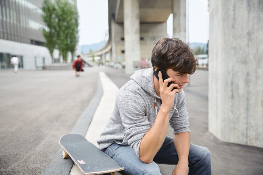 Junger Mann ist am Telefon und sitzt mit Skateboard auf einer Treppe.