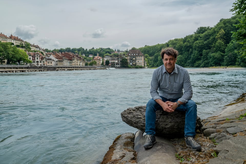 Andreas Zischg, Co-Leiter des Mobiliar Lab für Naturrisiken, sitzt auf einem Stein am Aareufer in Bern.