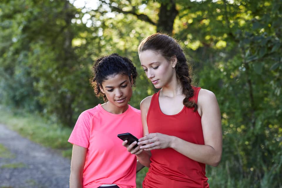 Zwei Frauen schauen beim Joggen auf ein Handy.