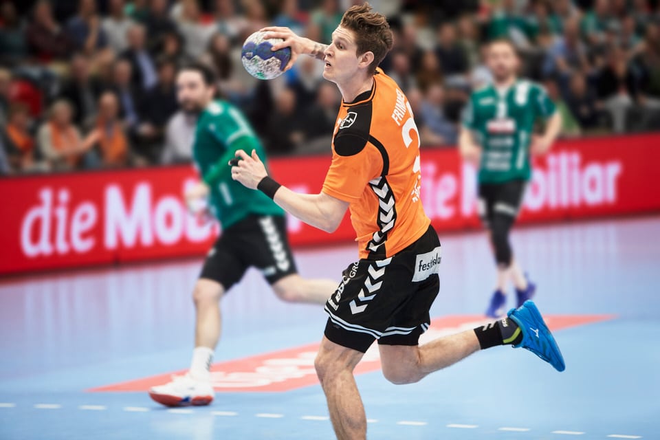 Handballspieler in orangem Trikot mit Mobiliar Sponsoring setzt zum Torwurf an