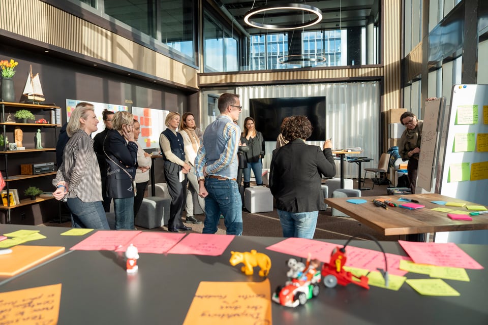 Un groupe de travail se tient dans la salle pour discuter ensemble de leurs idées. Les post-it sont au premier plan.