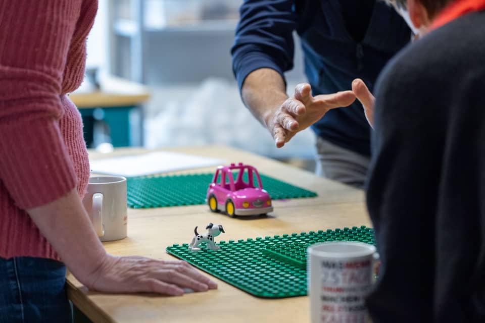 Photo de participantes et de participants autour d’une table sur laquelle sont posées des tasses ainsi que des plaques de base et des figurines LEGO.