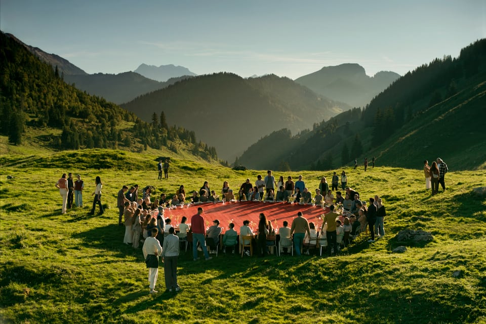 Eine Gruppe von Leuten sitzen an einem grossen roten runden Tisch auf einer grünen Wiese