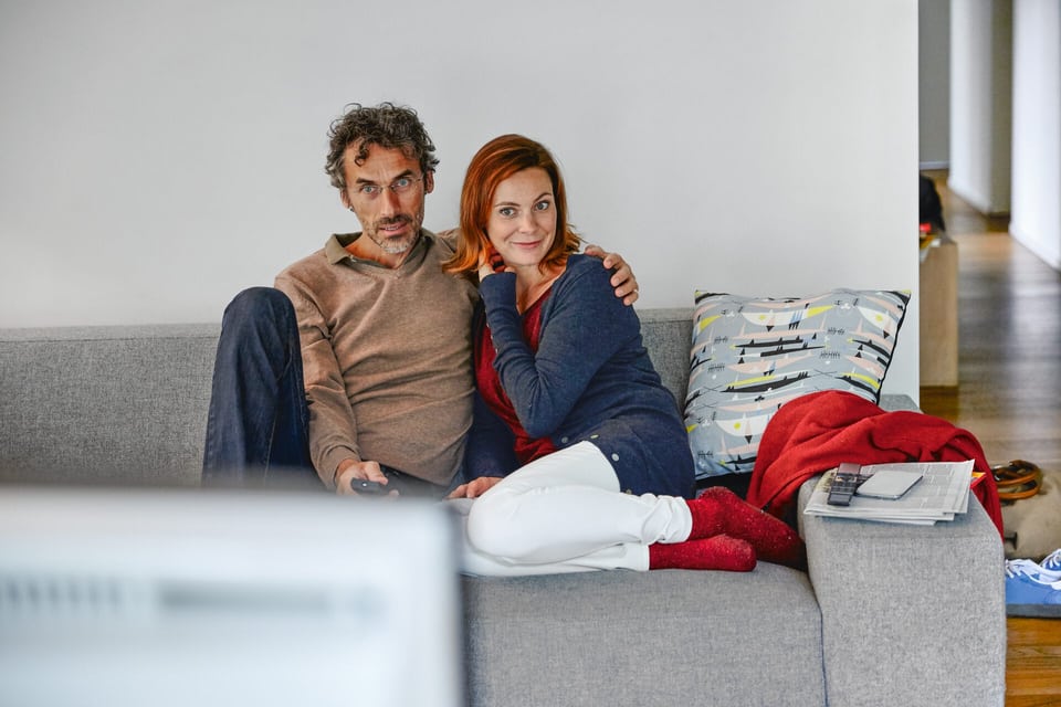 Ein junges Paar sitzt auf dem Sofa Arm in Arm.