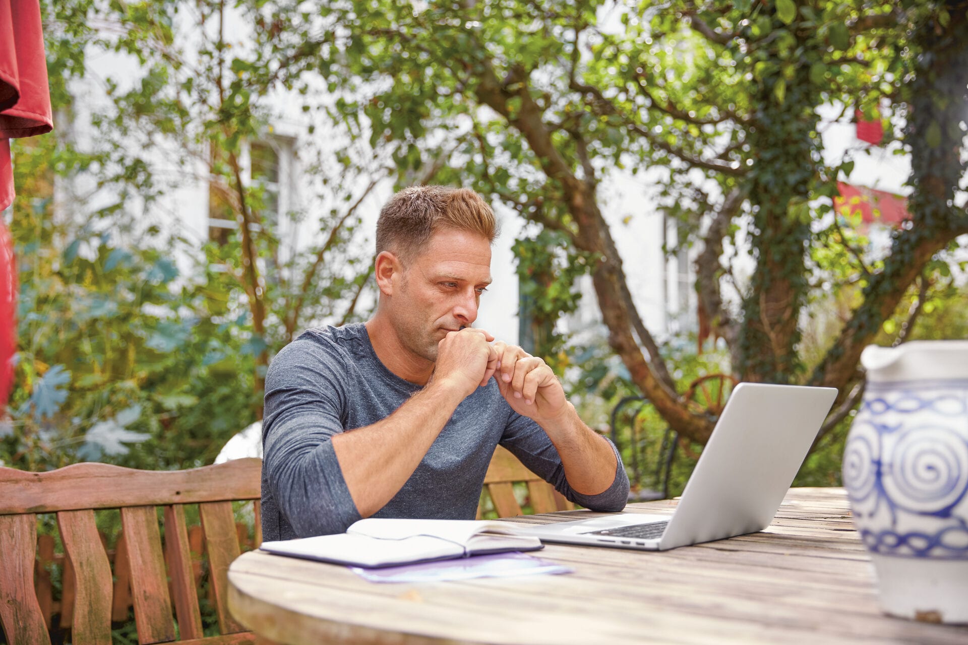 Ein Mann sitzt im Garten, vor ihm ein aufgeklappter Laptop, und recherchiert zum Thema Änderungskündigung Schweiz.