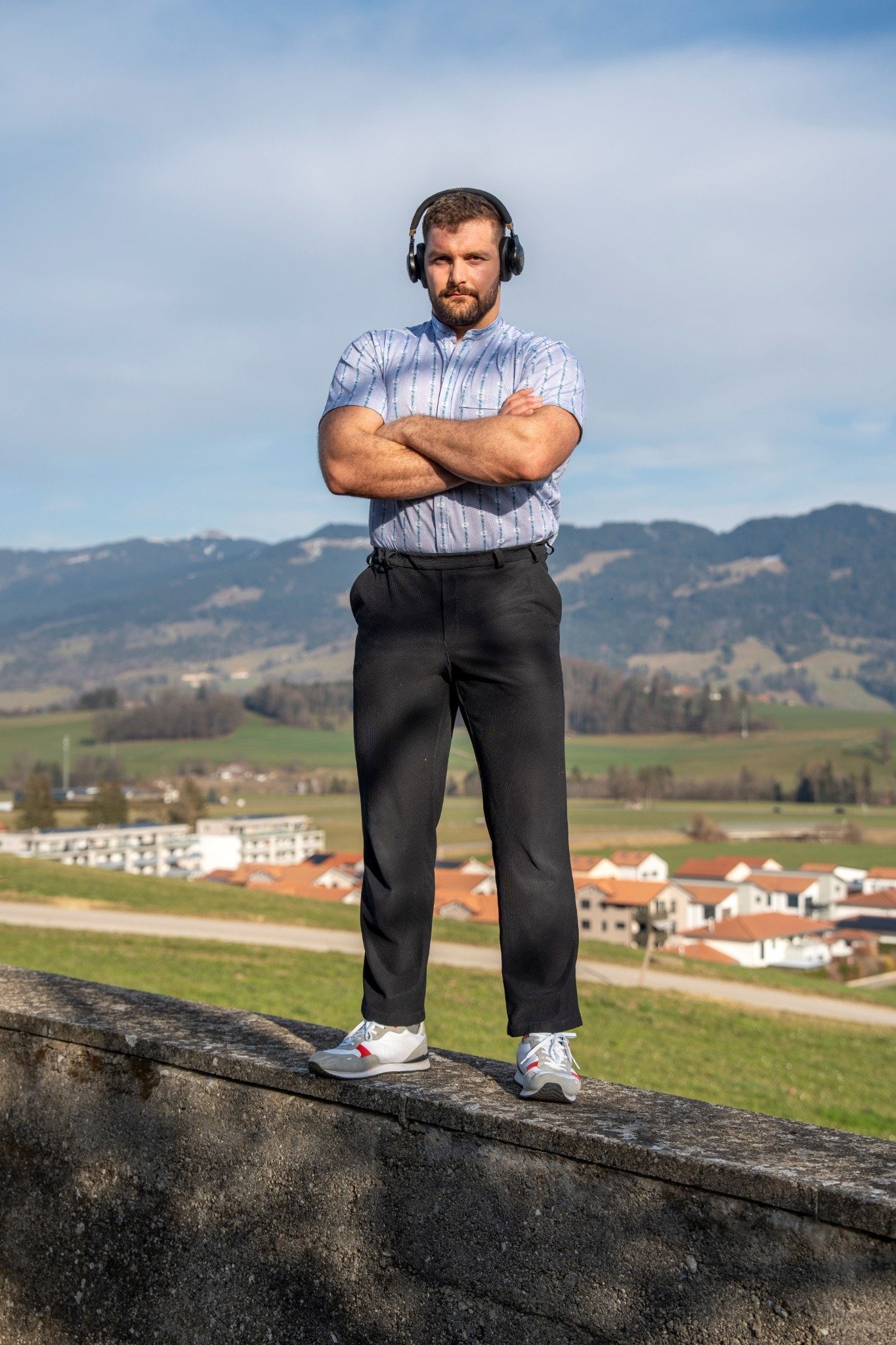 Benjamin Gapany, bras croisés et écouteurs sur les oreilles, se tient concentré sur un muret avec vue sur la campagne fribourgeoise.