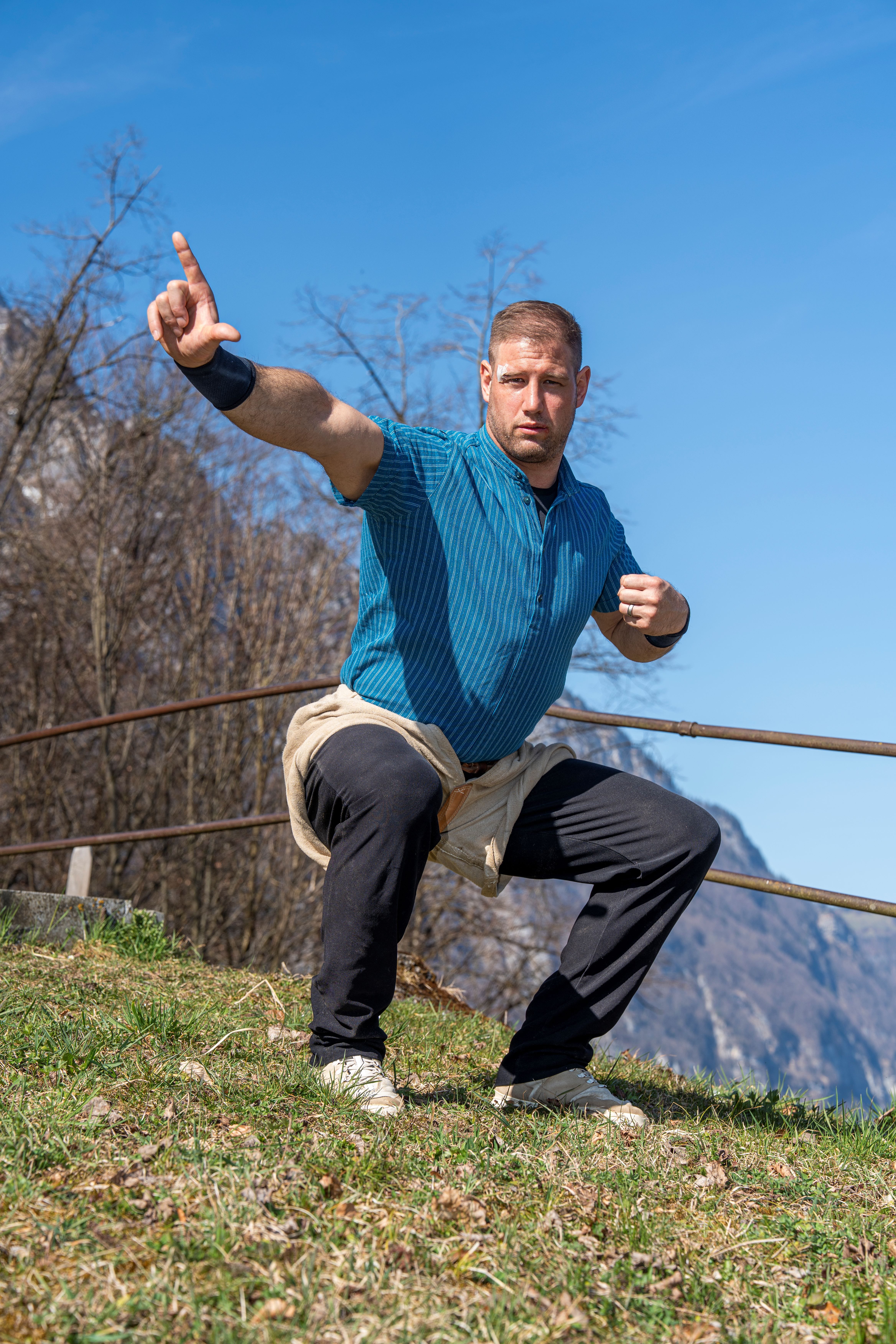 Roger Rychen in una posa di allenamento dinamica su un prato di fronte a una montagna – determinato, concentrato e in movimento.