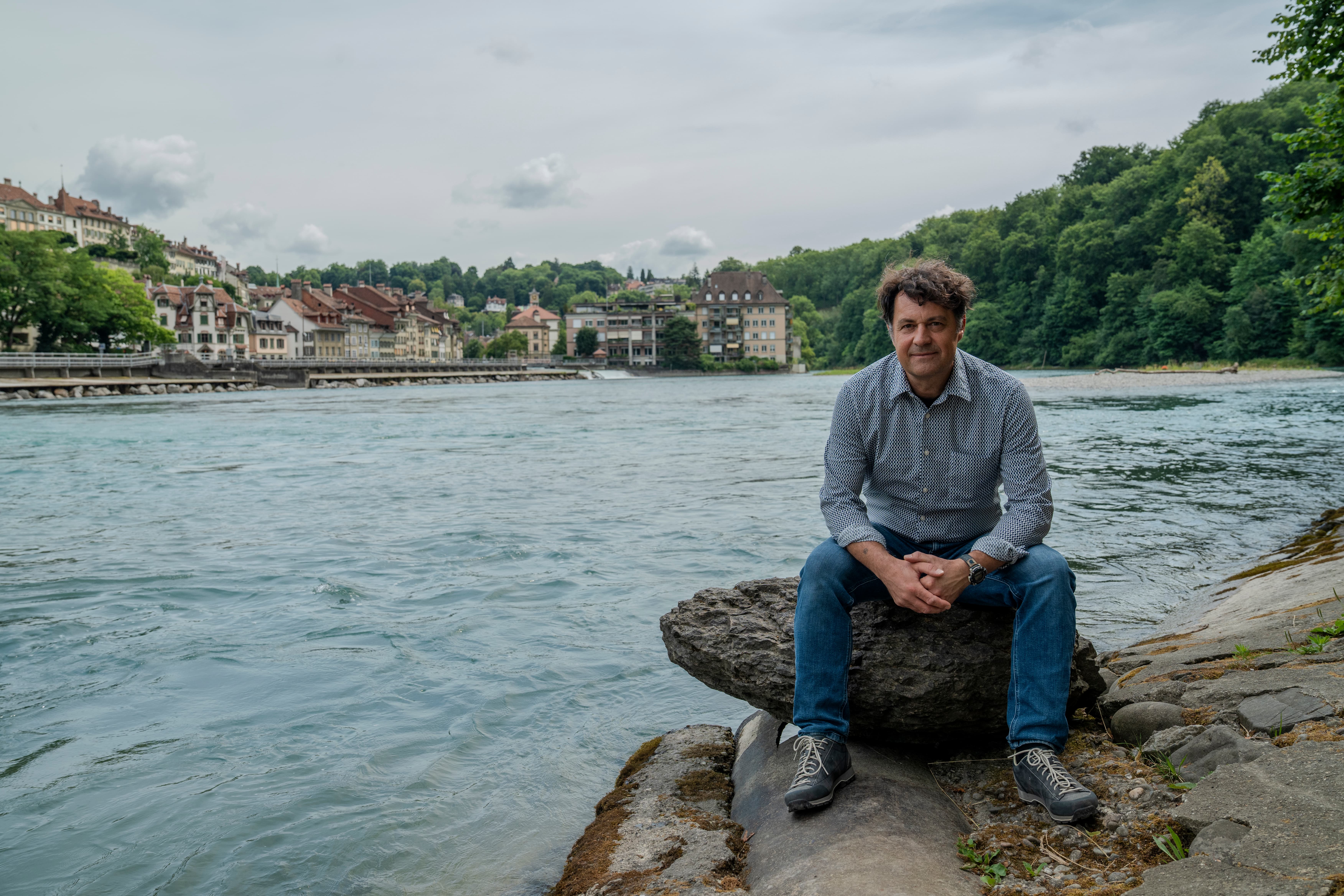 Andreas Zischg, Co-Leiter des Mobiliar Lab für Naturrisiken, sitzt auf einem Stein am Aareufer in Bern.