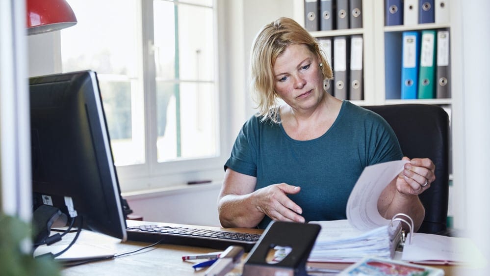 Eine Frau sitzt in einem Büro und blättert ein Dossier um.